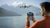 Man operating drone with remote controller over a lake with mountainous background