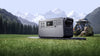 Portable power station stood on grass with two people in the background surrounded by mountains and trees