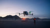 DJI Matrice 4 drone flying with a person standing near a vehicle with lights in the background at night