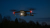 Drone with spotlight flying at night with trees in the background