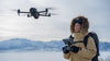 Woman operating a remote controller with Mavic 4 Pro drone flying near her in snowy landscape