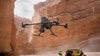 DJI Matrice 400 enterprise drone flying in canyon with men standing in the background near a yellow car