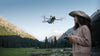 Woman wearing hat operating a Mini 4 Pro drone with a natural mountainous background