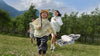 Family running in field with DJI Neo grey drone flying in the foreshot of the photo surrounded by trees and mountains