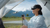 Woman with FPV goggles operating the DJI Neo drone against a mountainous background