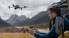 Man operating a grey DJI drone with a mountainous background