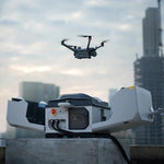 Matrice drone flying above an open DJI Dock 3 station with buildings in the background