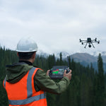 Man operating remote controller with Matrice enterprise drone flying in the background with a natural setting