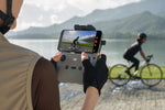 Person operating RC-N3 remote controller for a drone to record a cyclist by a lake.