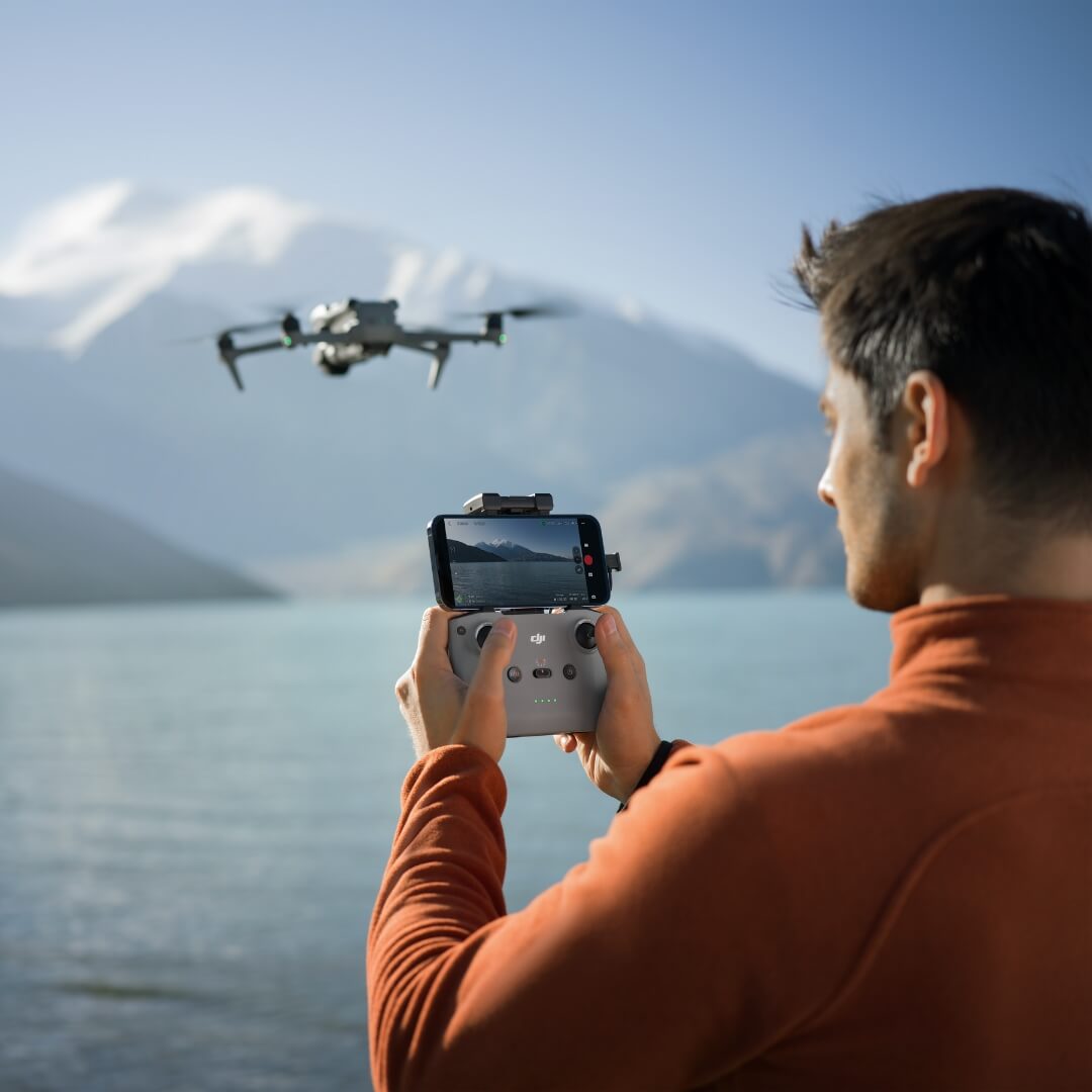 Person operating a DJI Air 3S drone with an RC-N3 controller over a scenic lake and mountain backdrop