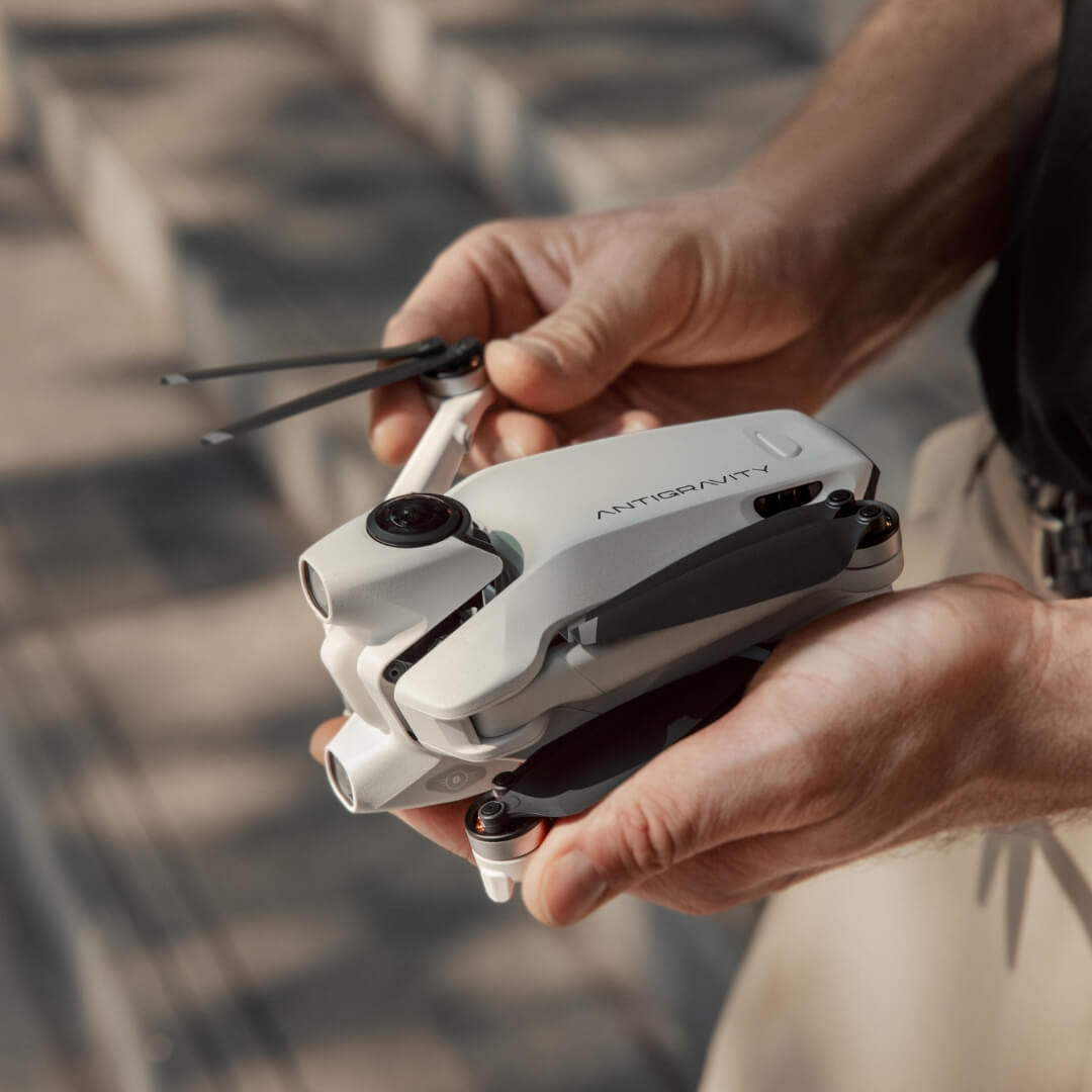 Person holding a folded white drone with 'Antigravity' branding against a blurred background