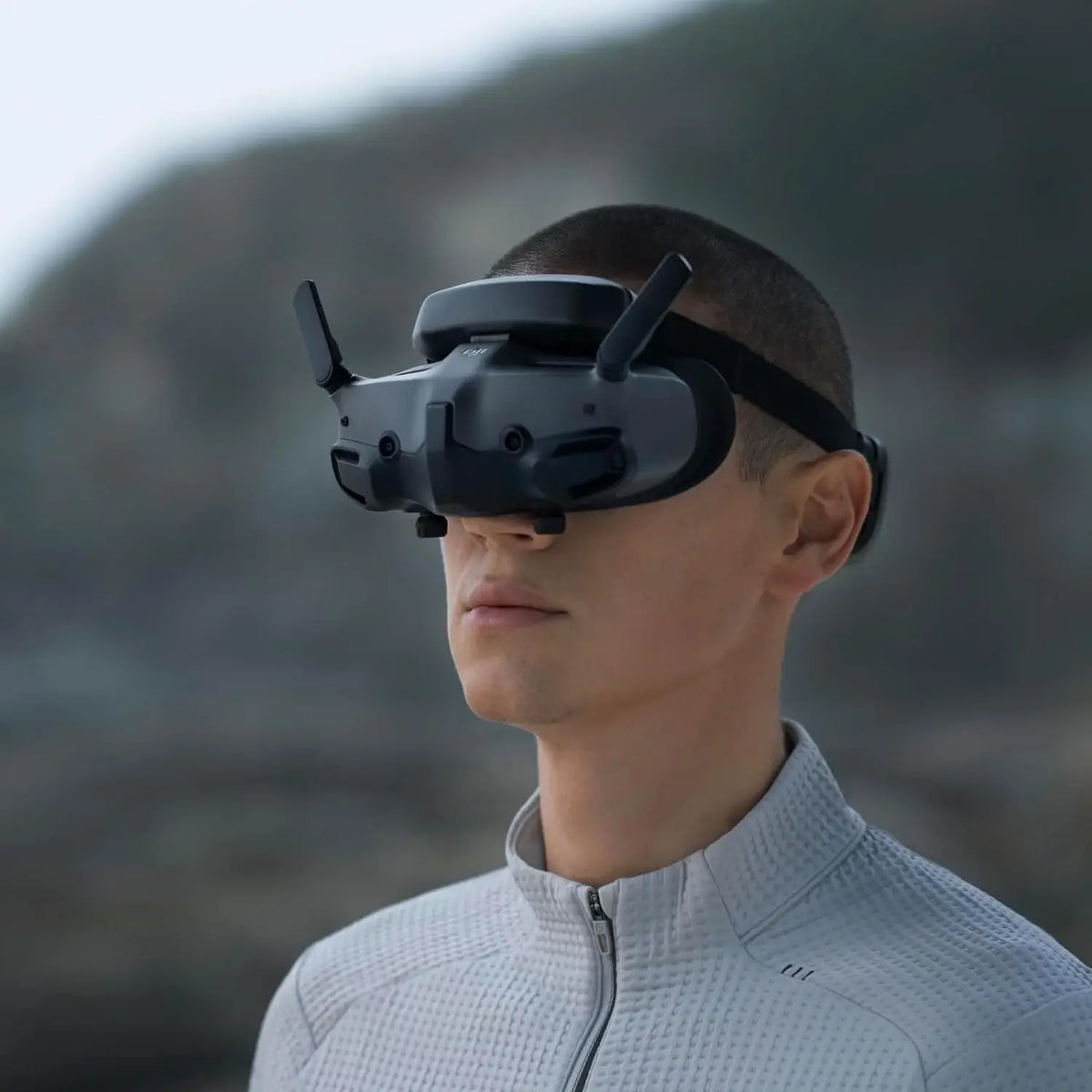 A man wearing the dji fpv goggles 3 with a mountainous background