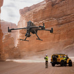 Large Matrice 400 enterprise drone flying over a desert landscape with a person and vehicle in the foreground