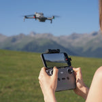 Person operating a DJI Mini 5 Pro drone with an RC-N3 controller in a scenic outdoor setting with mountains