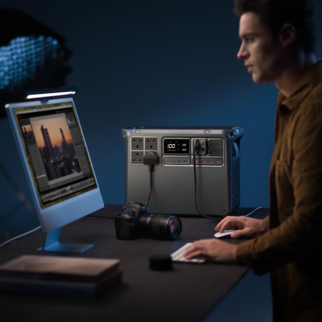 Person working at a desk with a computer, power station and camera
