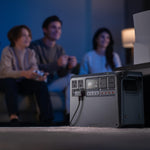 Portable Power 2000 station on a carpeted floor with people playing video games in the background