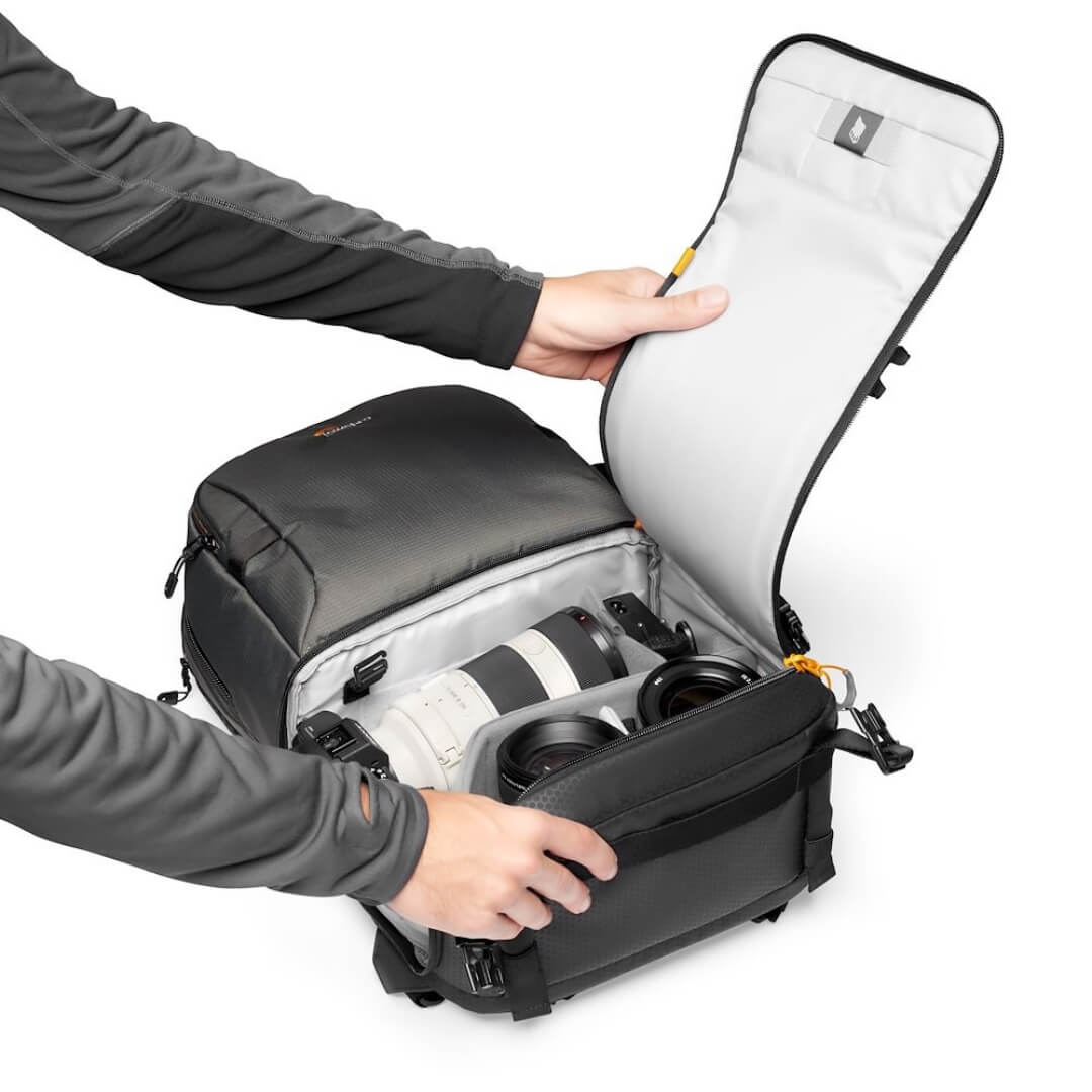 Person opening a black backpack with camera equipment inside on a white background