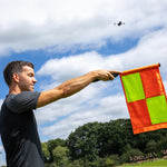 Man holding a flag outdoors with trees and sky in the background