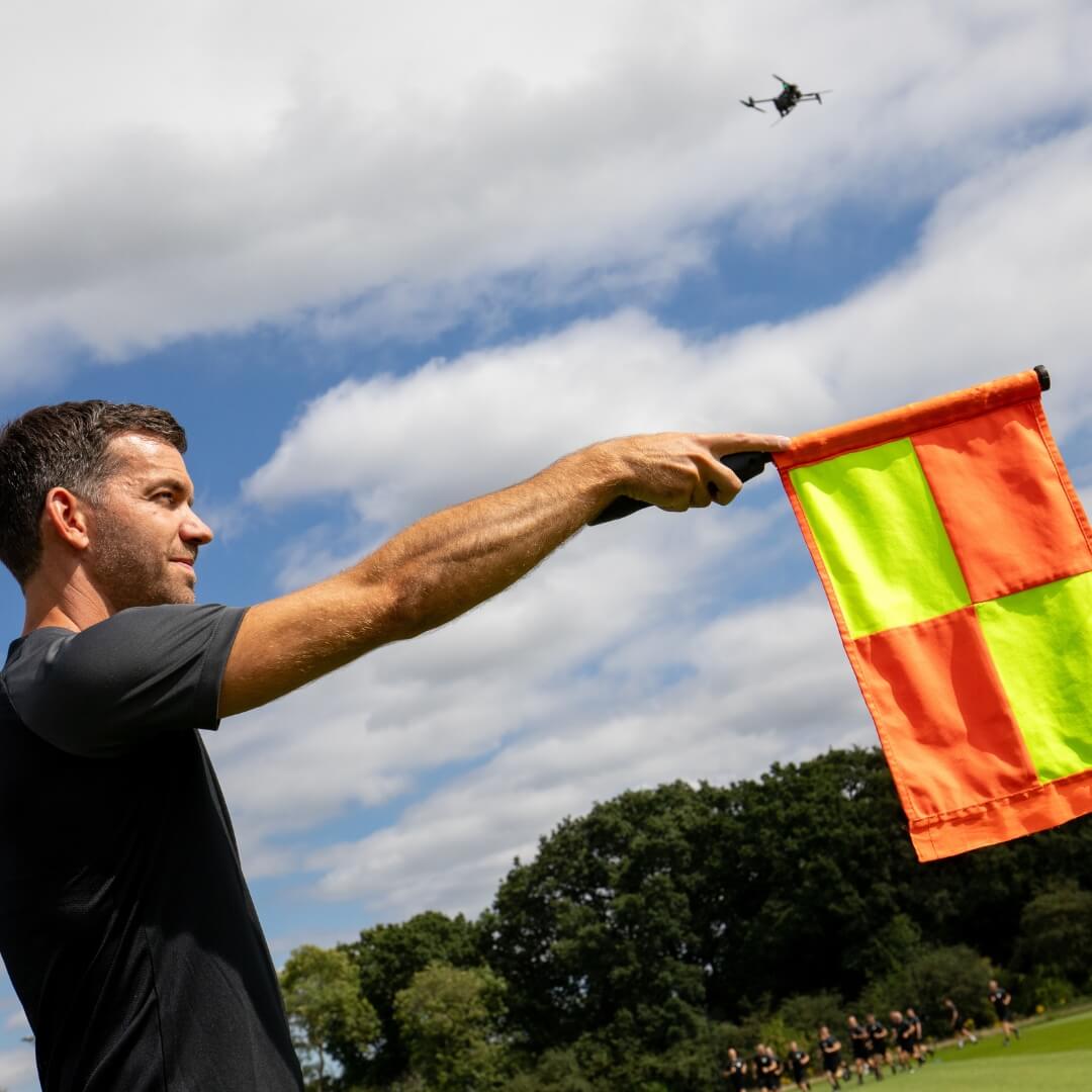 Man holding a flag with a drone flying above on a sunny day