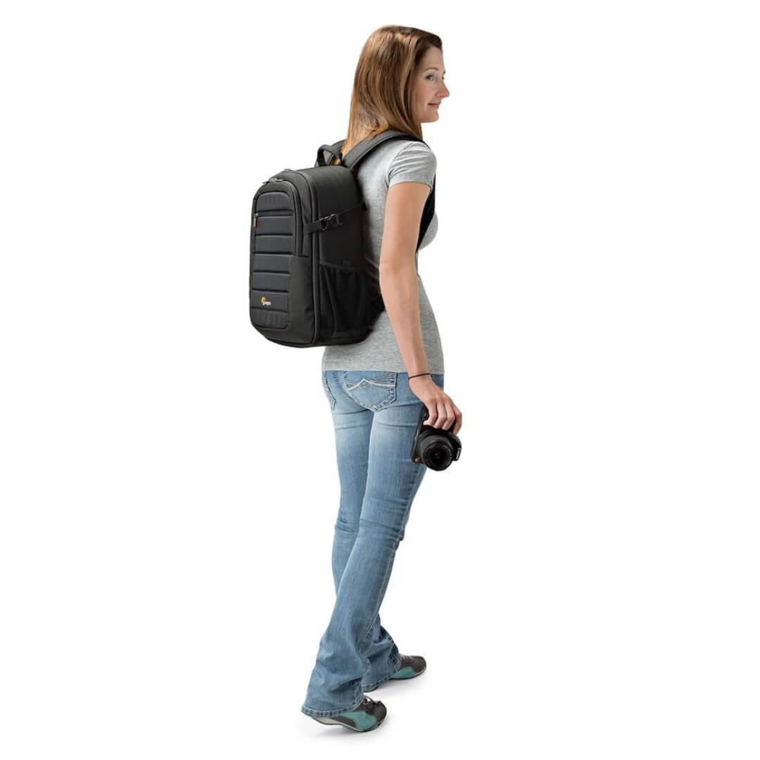 Woman wearing a black backpack and holding a camera against a white background
