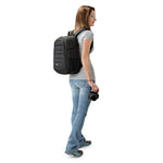 Woman wearing a black backpack and holding a camera against a white background