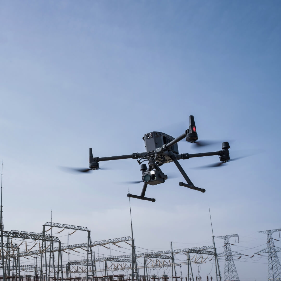Drone flying over power plant structures against a clear blue sky