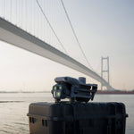 DJI Matrice 4E drone folded on a black box with a bridge and water in the background