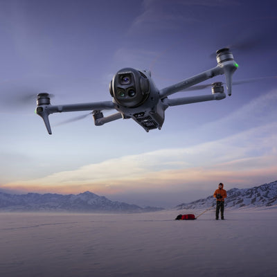 Drone flying with man operating controller in background with snowy landscape
