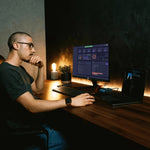 Man sitting at a desk with a computer setup in a dimly lit room using drone operations management software