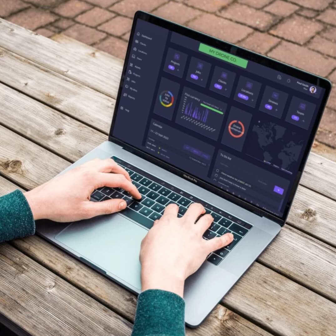 Person using drone operation management software with laptop on a wooden table with a brick floor in the background