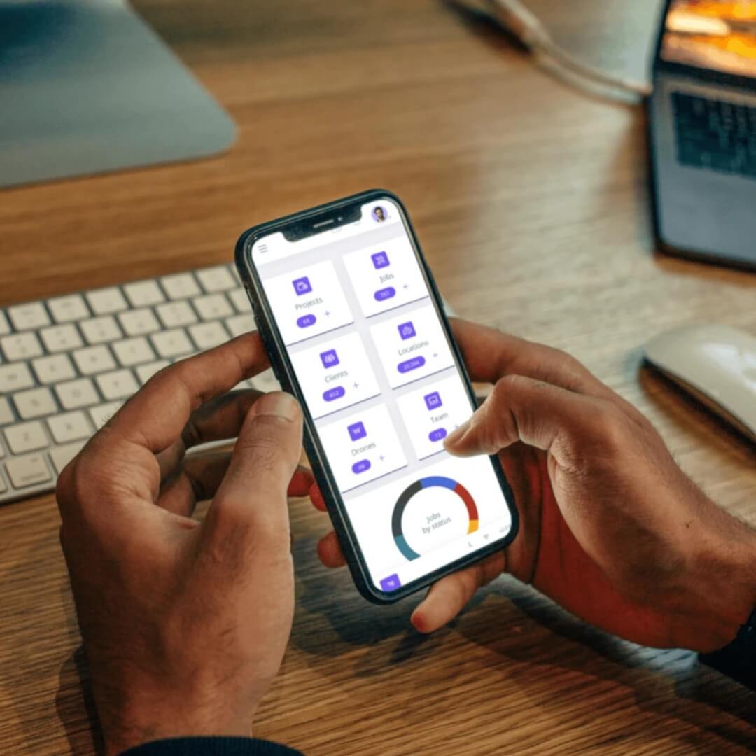 Person using a smartphone app on a desk with a keyboard and laptop in the background