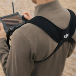 Person wearing a shoulder harness with a DJI logo on it whilst holding a controller