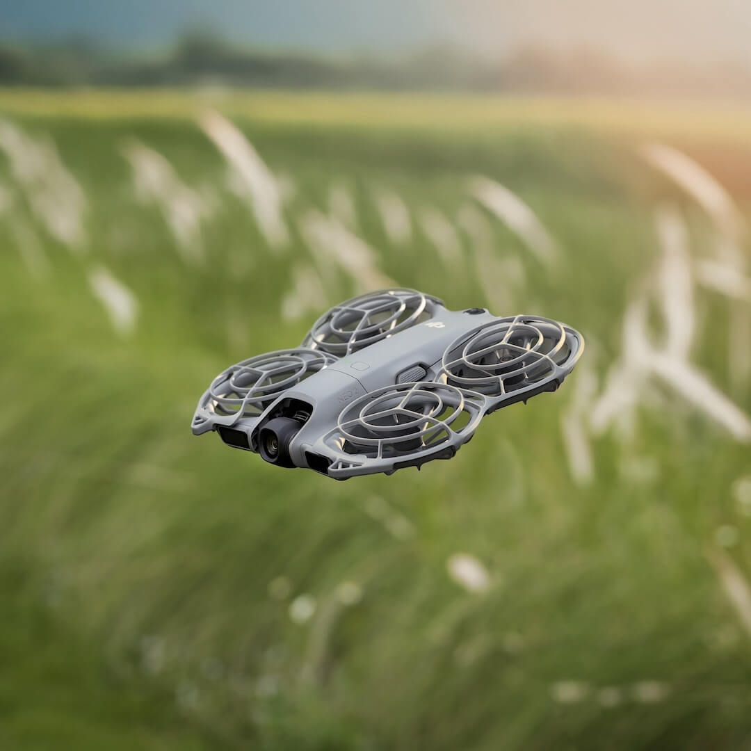 Gray drone hovering over a grassy field with a blurred background