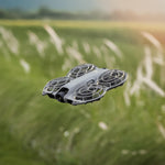 Gray drone hovering over a grassy field with a blurred background