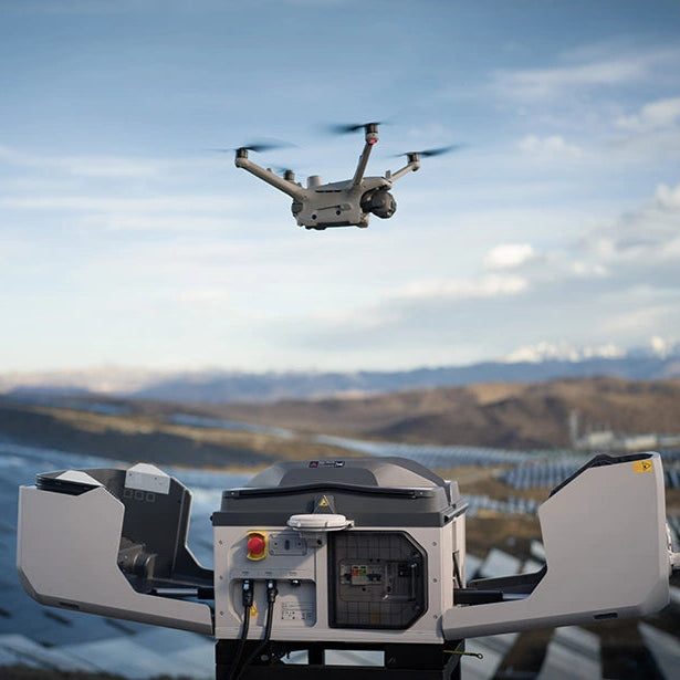 Matrice drone flying above open DJI Dock 3 station with a mountainous background