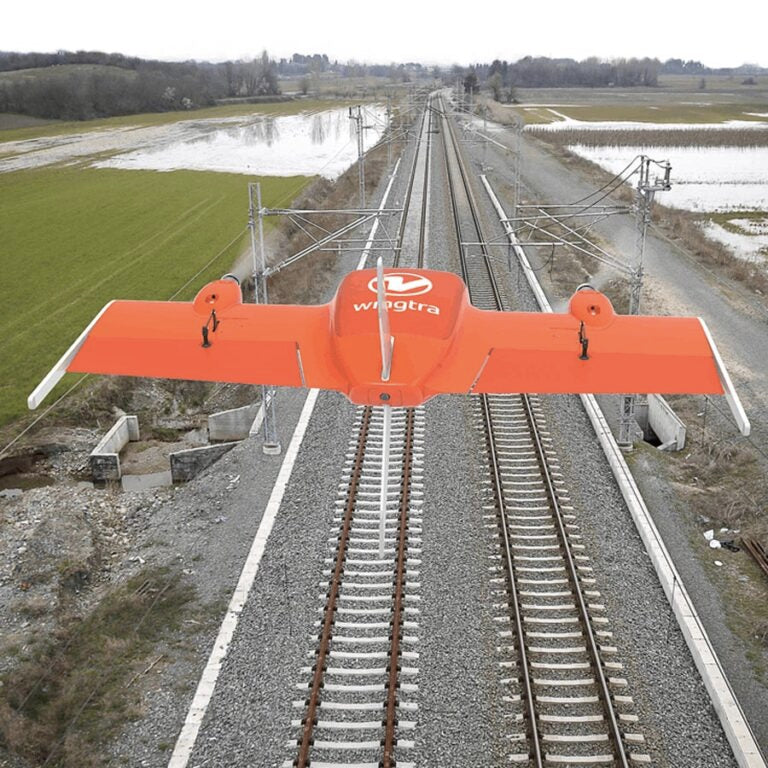 Orange Wingtra drone flying over a railway track with flooded grasslands on both sides of the track