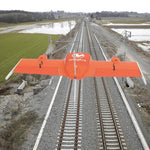 Orange Wingtra drone flying over a railway track with flooded grasslands on both sides of the track