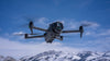 Bottom-up view of DJI Mavic 4 Pro drone flying with a snowy mountainous landscape in the background