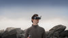 Man wearing FPV goggles with controller and rocks in the background