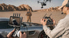 Two men operating a drone on a film set alongside a car in a desert setting