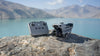 Folded grey drone and remote controller sat on a rock with a lake and mountain in the background