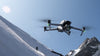 DJI Air 3s grey drone flying above snowy mountain with blue sky and sun in the background