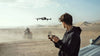 Man operating a drone with anothe rperson on a bike in the background in the desert