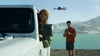 Man operating a drone near lake with woman in car sticking her head out of the window