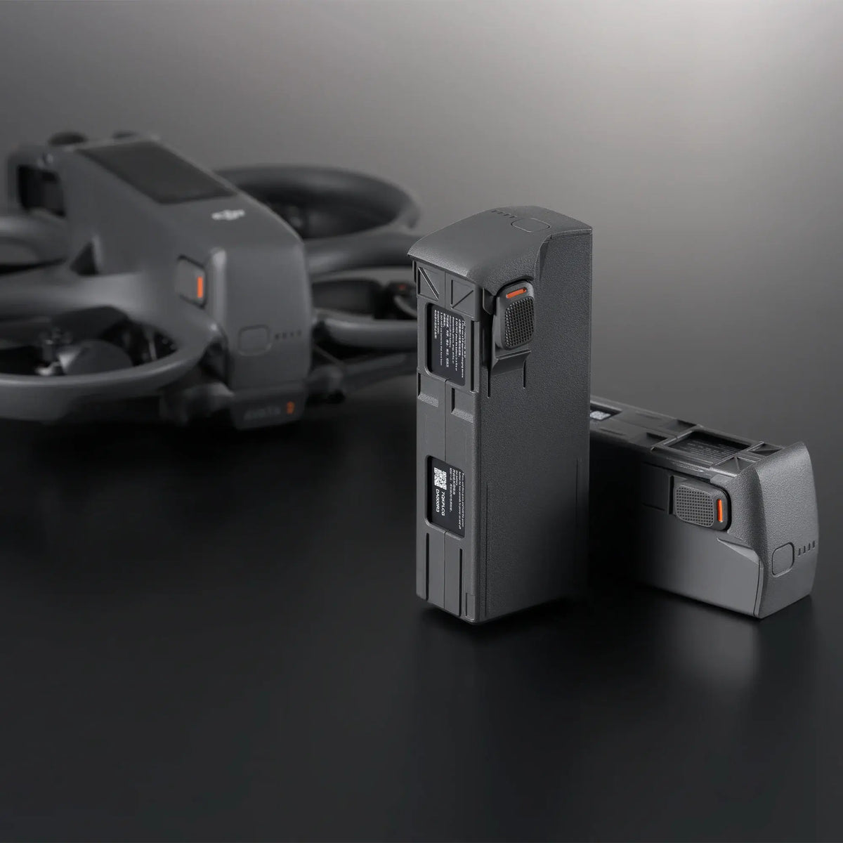 Two drone batteries on a dark surface with a blurred Avata 2 drone in the background