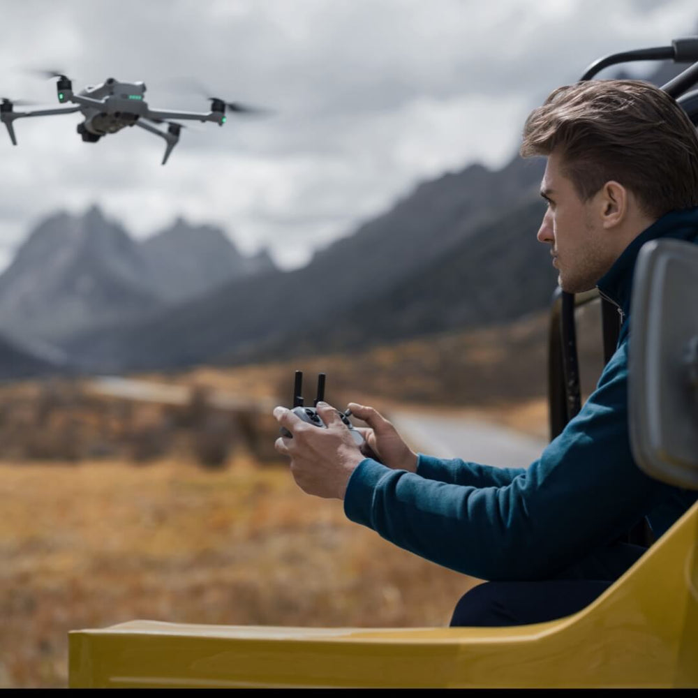 Drone pilot using a handheld controller outdoors with a mountain landscape behind him