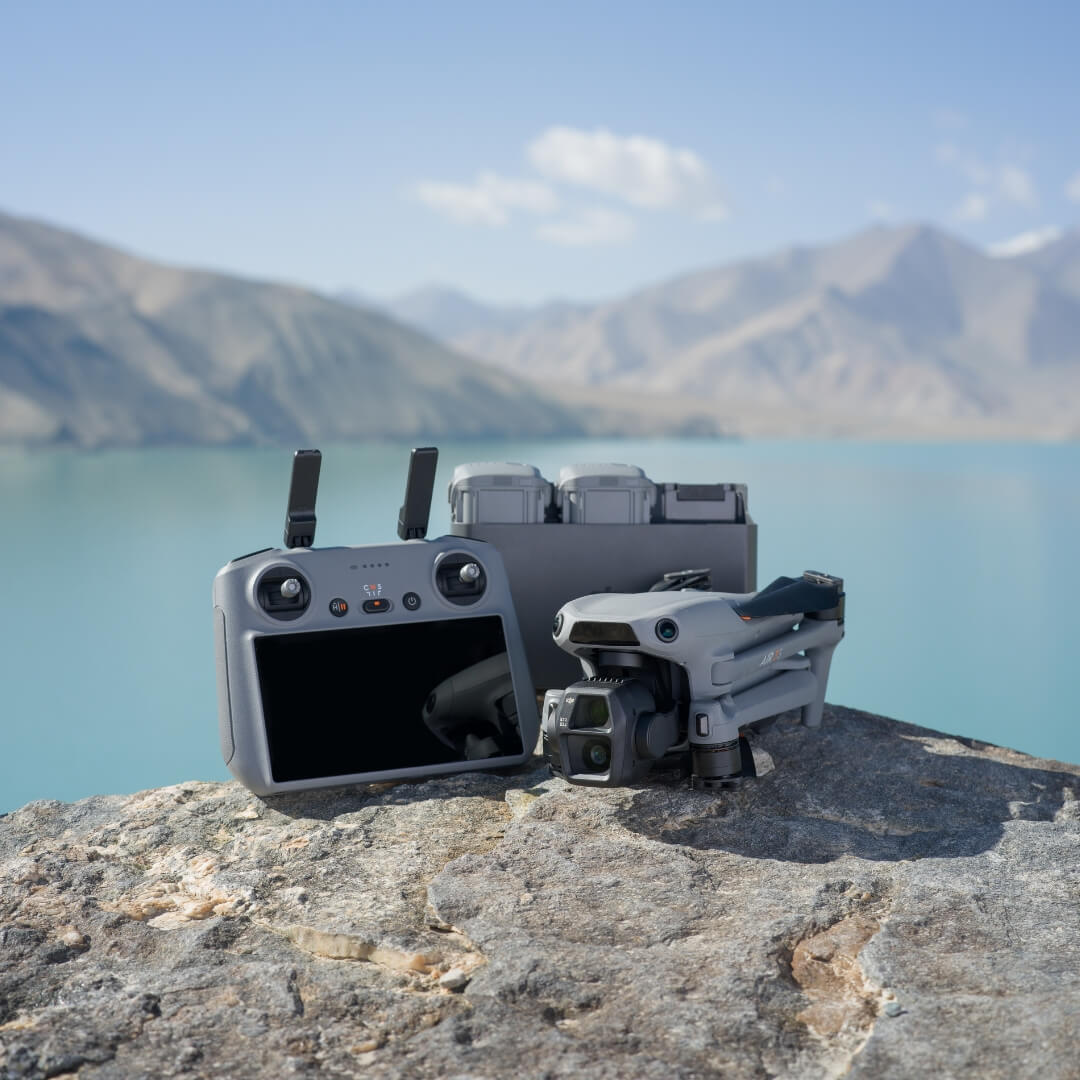 DJI Air 3S drone, RC 2 controller and three drone batteries on a rock with a mountainous landscape in the background