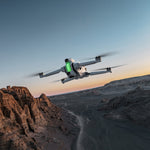 Unmanned aerial drone flying over a desert landscape with a sunset