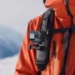 Action camera mounted on a backpack with a person wearing an orange jacket in the background.