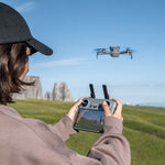 Person operating a DJI Mini 5 Pro grey drone with an RC 2 controller in an open field